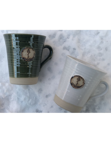 Handdrejad mugg i vit eller gräsgrön glasyr med emblem föreställande Jämtlands landskapsblomma, Brunkullan.