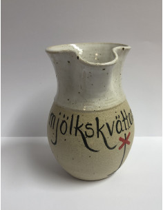 En drejad liten kanna med texten Mjölkskvätten och ett målat ledkryss